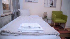 A neatly made bed with folded white linens, a green chair, and a small table with a lamp. - Comfortable single room with shared bathroom  (Plauen)