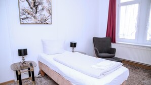 A hotel room with a bed, a chair, a table with lamps, and a window with curtains. - Comfortable single room with shared bathroom  (Plauen)