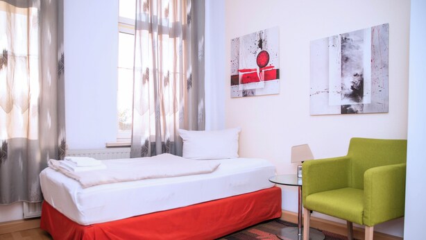 A hotel room with a bed, a green chair, a small table, and two abstract paintings on the wall. - Comfortable single room with shared bathroom  (Plauen)
