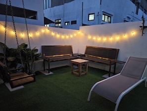 An outdoor seating area with a swing chair, two wooden benches, and a lounge chair.