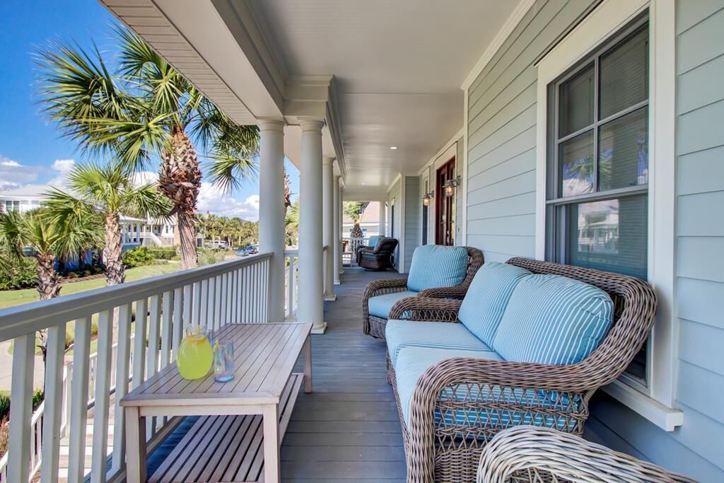 A covered porch with wicker furniture and a table, overlooking a lawn with palm trees.