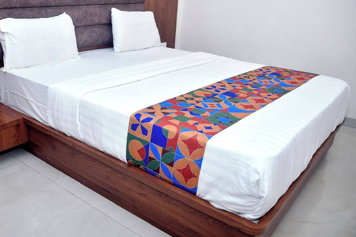 A bed with a wooden frame, white bedding, and a colorful geometric-patterned throw.