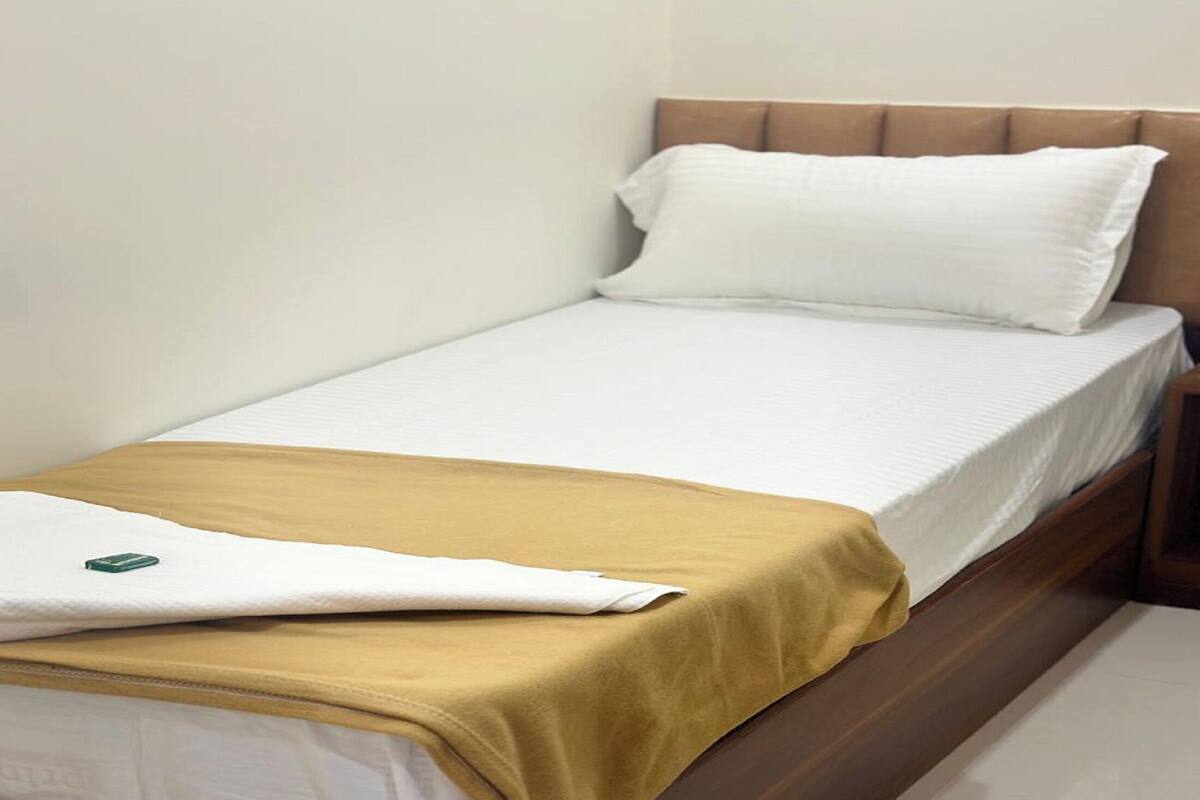 A single bed with a wooden frame, white bedding, and a mustard-colored blanket.