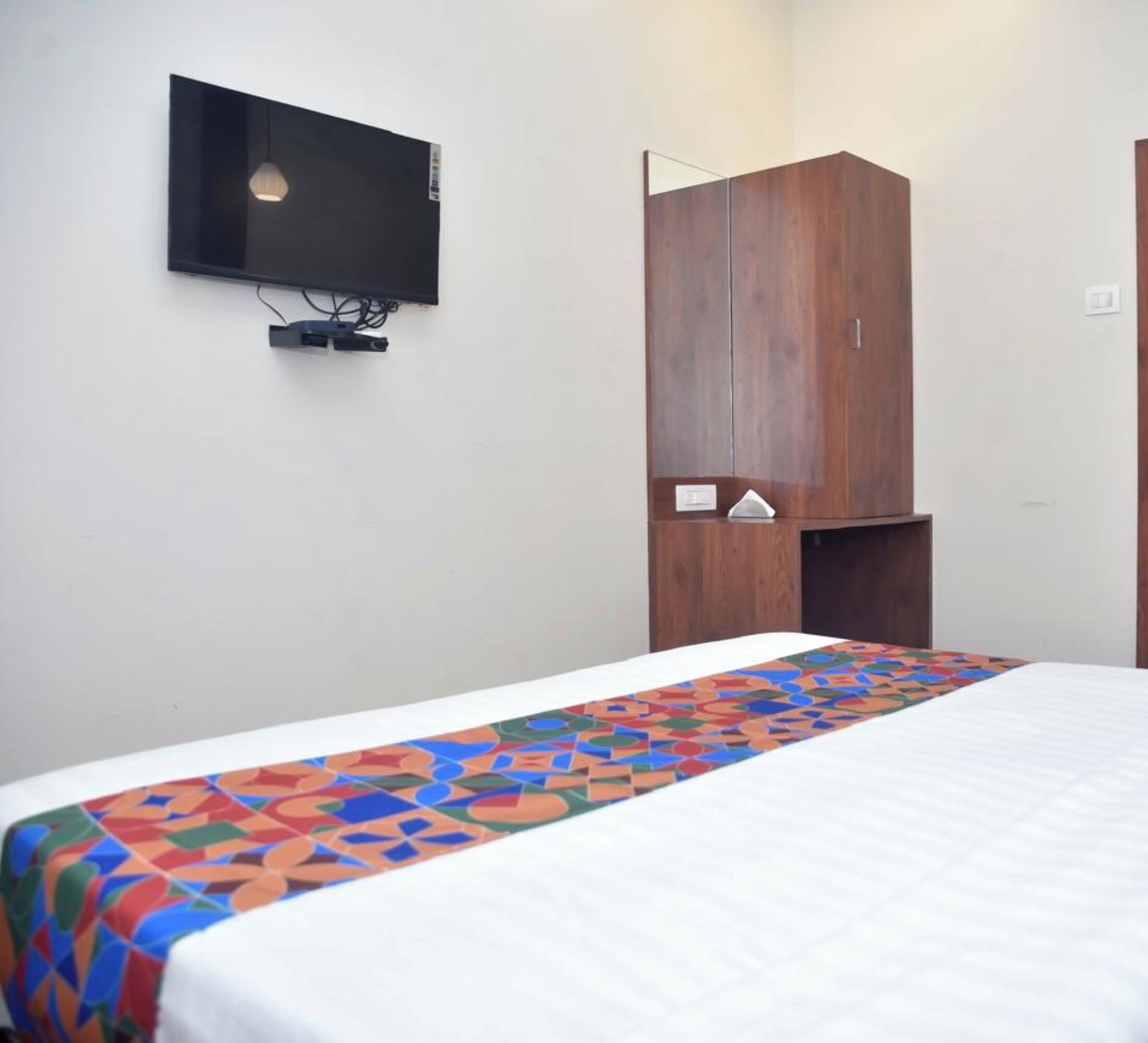 A bedroom with a bed, a TV mounted on the wall, and a wooden wardrobe.