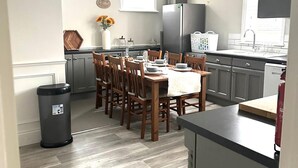 A modern kitchen with a dining table set for six, wooden chairs, a trash bin, and a refrigerator. - Luxury Family Home Central Bournemouth Sleeps 6 (Bournemouth)