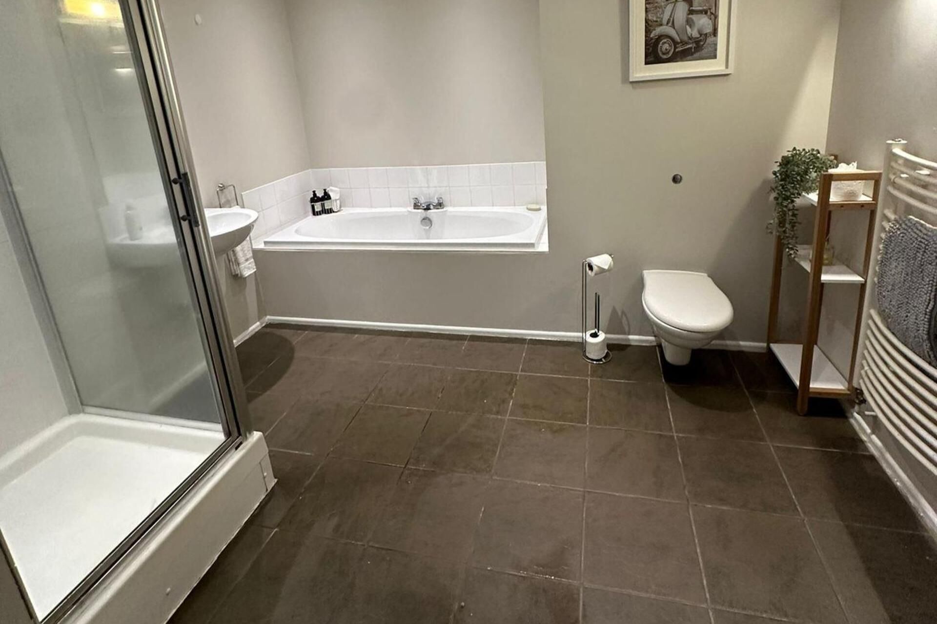 A bathroom with a glass shower enclosure, a bathtub, a toilet, and a small sink.