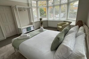 A bedroom with a large bed, a chair, a wardrobe, and a window with blinds.