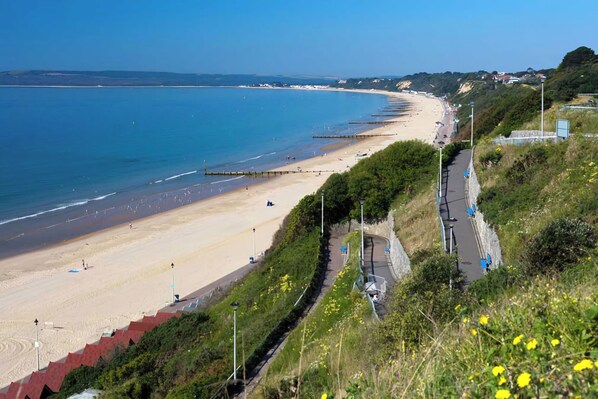 A coastal road with a beach on one side and a green hillside on the other.