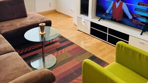Un salon comprenant un canapé, une table basse en verre, un tapis à motifs, un téléviseur et un meuble.
