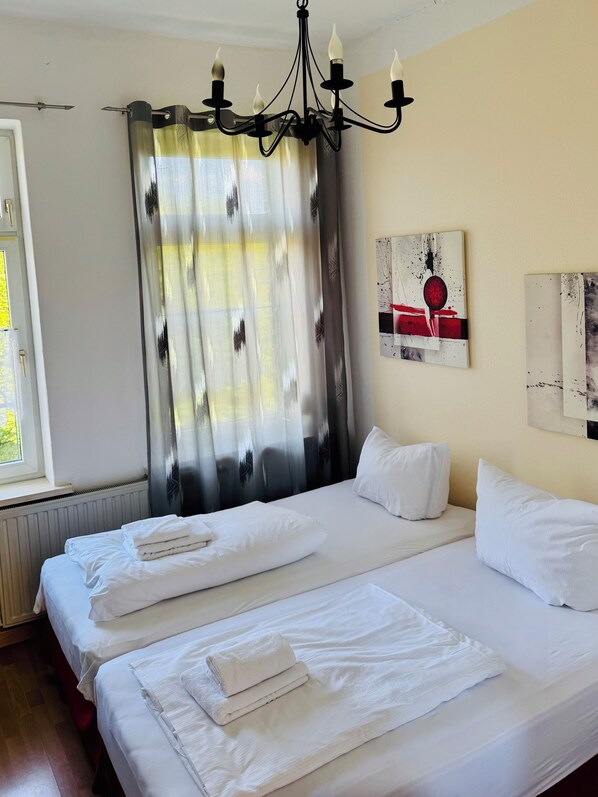 Una habitación de hotel con dos camas, una araña, una ventana con cortinas y obras de arte en la pared.