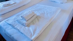 Une chambre d’hôtel avec deux lits, du linge de lit blanc et des serviettes. Les murs sont ornés de tableaux abstraits.