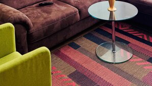 Un canapé en cuir marron, une petite table ronde en verre et un tableau abstrait aux couleurs vives accroché au mur.