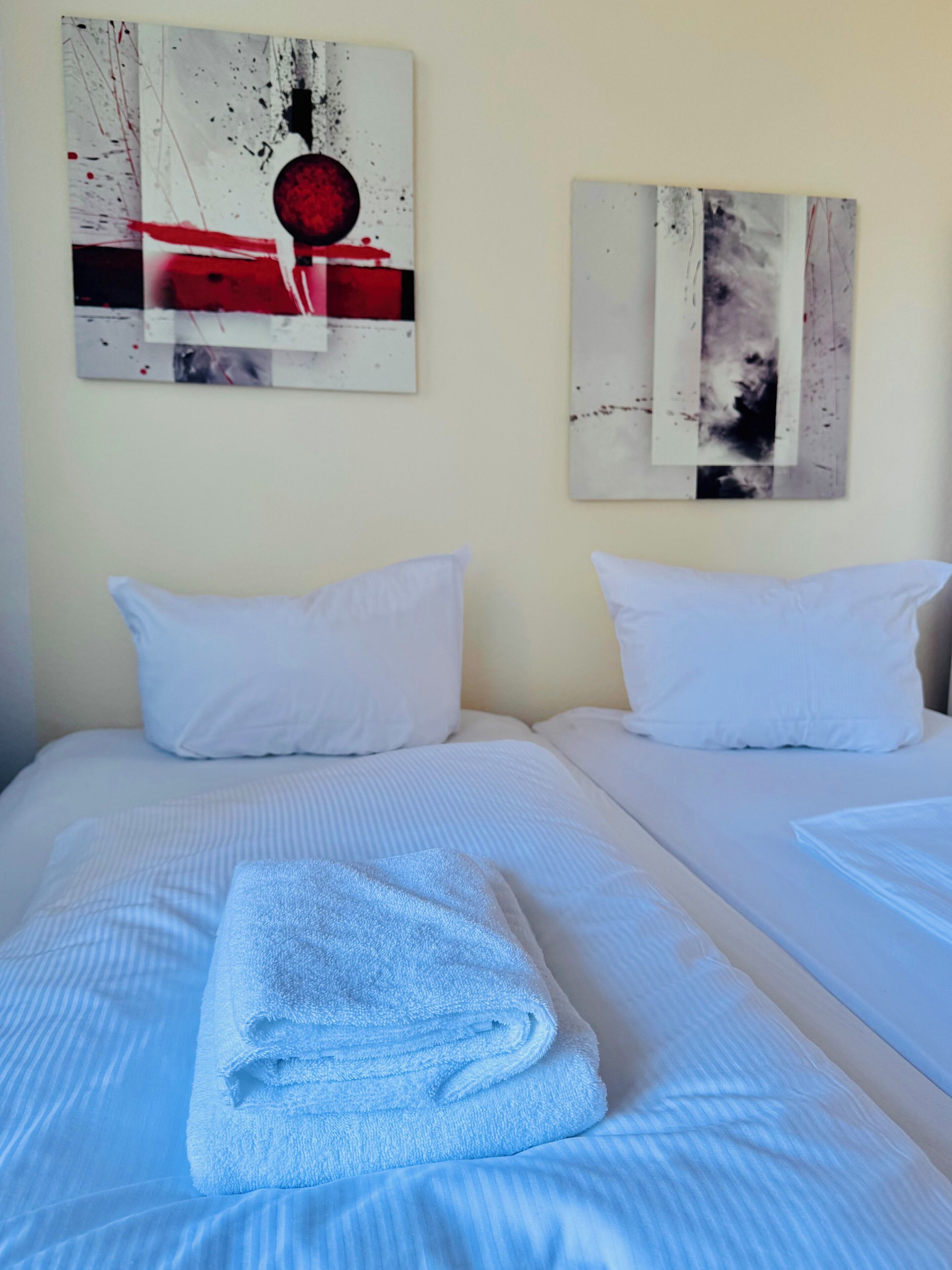 Ein Hotelzimmer mit zwei Betten, weißer Bettwäsche und Bildern an den Wänden.
