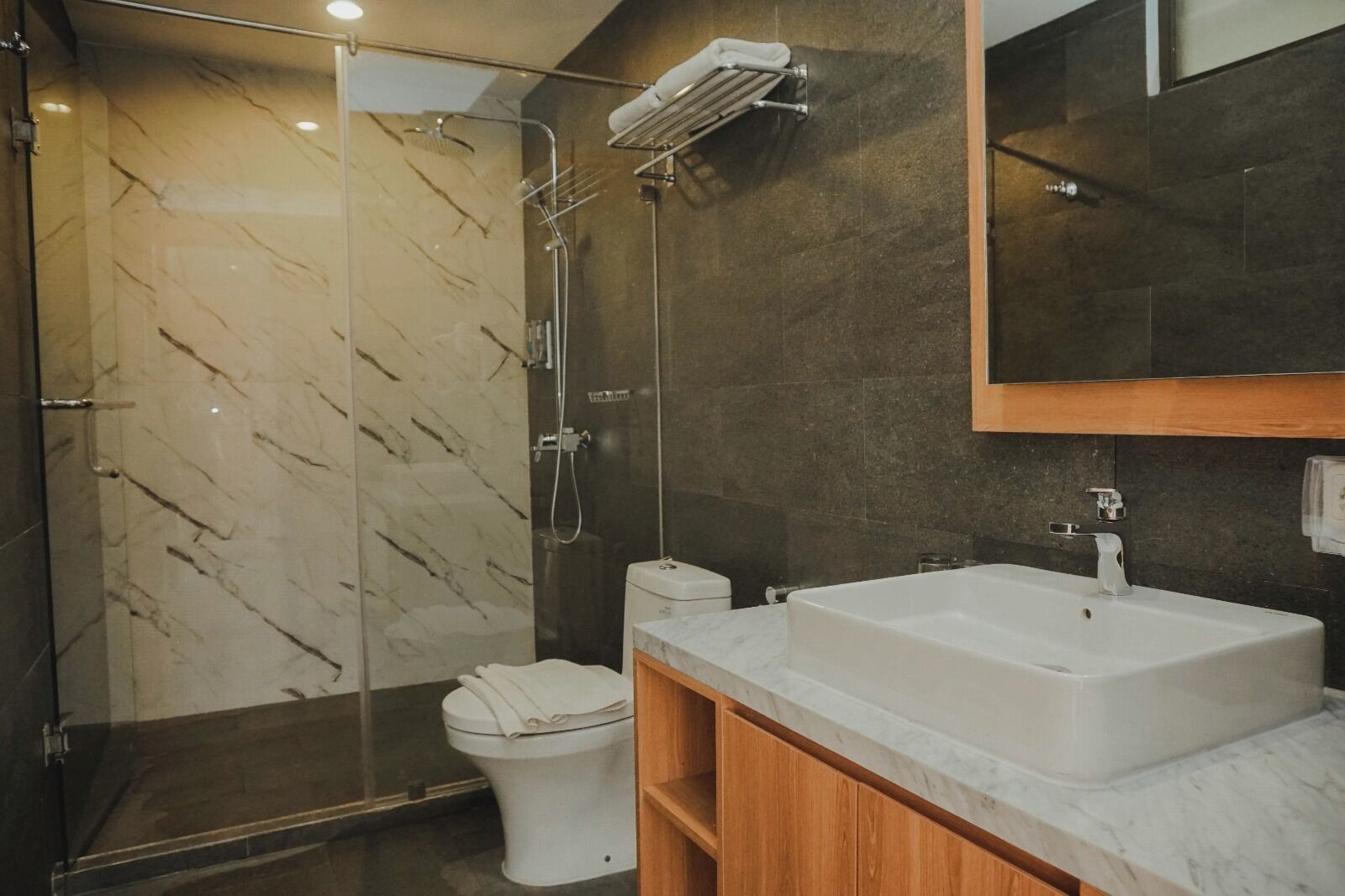 Ein modernes Badezimmer mit einer Duschkabine, einer weißen Toilette und einem großzügigen Waschbecken mit Holzschrank.