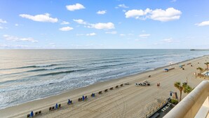 A beach with a long stretch of sand, a pier in the distance, and a clear sky. - Garden City Beach Oceanfront Condo 508 | Rising Tides Properties Rental (Murrells Inlet)