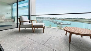 Een balkon met een bank en een houten tafel, met uitzicht op een jachthaven met boten.