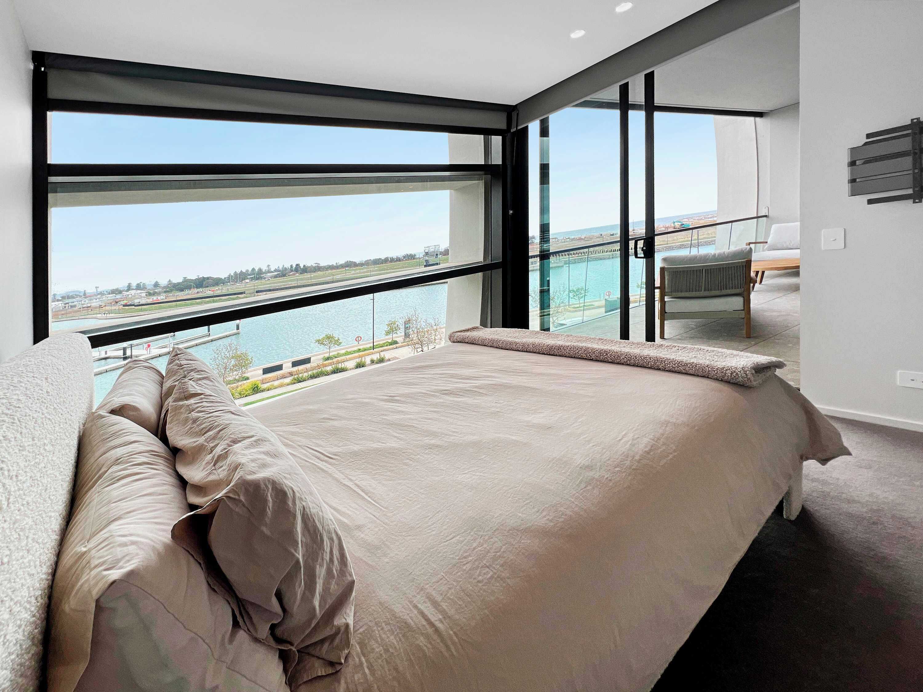 A modern bedroom with a large bed, a view of a body of water, and a balcony with a chair.