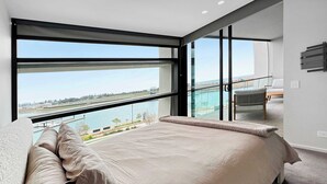 Een moderne slaapkamer met een groot bed, uitzicht op een waterpartij en een balkon met een stoel.