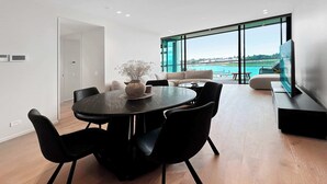Een moderne eetruimte met een ronde tafel, zwarte stoelen en een bloevas. Er is een groot raam met uitzicht op een wateroppervlak en gebouwen.