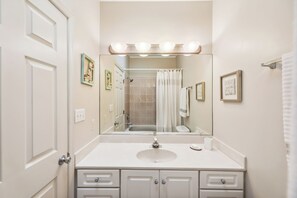 A bathroom with a white vanity, a sink, a mirror, and a shower curtain.