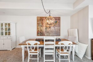 Un coin repas avec une table en bois, des chaises blanches, un lustre et un grand tableau abstrait accroché au mur.