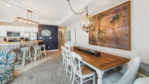 A modern kitchen with white cabinets, a wooden dining table, and a large abstract painting.
