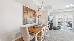 A dining area with a wooden table, chairs, a chandelier, a large abstract painting, and a television.