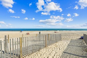 Une plage de sable bordée d’une clôture en bois, sous un ciel bleu et dégagé.