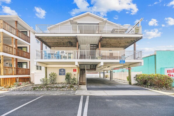 A multi-story building with balconies, a parking area, and a sign indicating availability for rent.