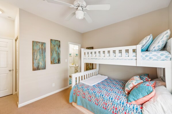 Une chambre d’enfant avec des lits superposés, un ventilateur de plafond et des œuvres d’art accrochées aux murs.
