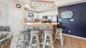 A kitchen with a central island, white cabinets, a stainless steel refrigerator, and a clock on the wall.