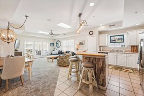 A spacious living area with a dining table, bar stools, and a kitchen with white cabinets.