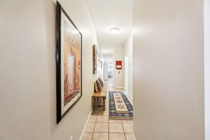Un couloir avec un tableau encadré sur le mur de gauche, une petite table avec des coussins et un tapis à motifs sur le sol.