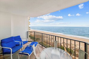 Ein Balkon mit Blick auf den Strand, einem Tisch und blauen Stühlen.