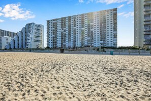 Una playa arenosa con modernos edificios altos al fondo.