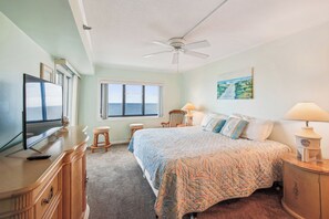 A bedroom with a bed, a TV, a ceiling fan, a window with a view, and a painting on the wall. - XPLORIE ACTIVITIES & LINENS INCLUDED*! Plaza 3BR/2BA oceanfront condo! Indoor/outdoor pools & Tiki Bar. (Ocean City)