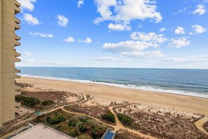 Une vue sur la côte, avec une plage de sable, un ciel dégagé et un bâtiment doté d’une architecture originale.