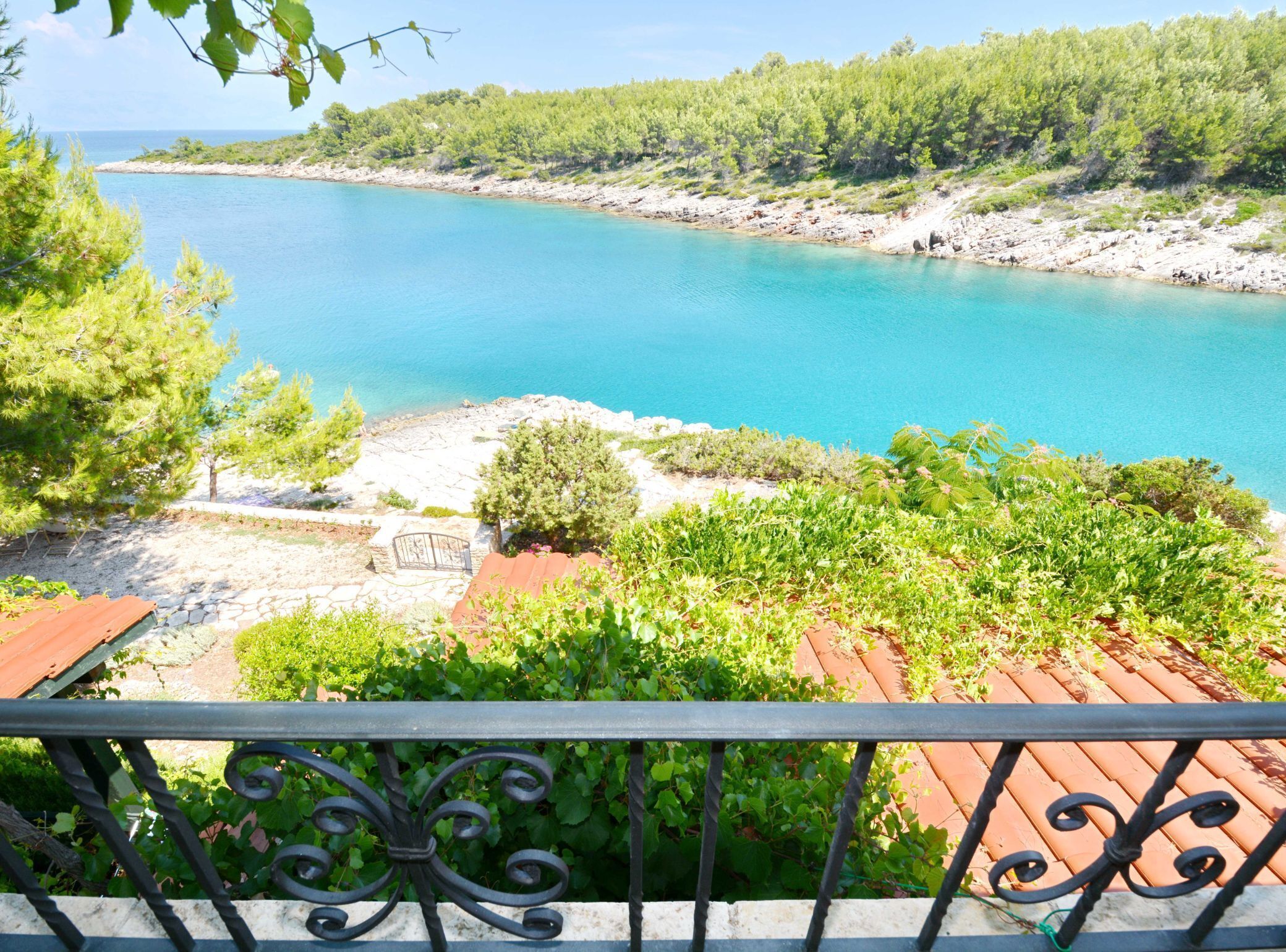 A coastal view with a clear blue sea, rocky shoreline, and lush greenery.