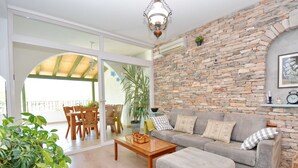 A spacious living room with a stone wall, a grey sofa, wooden furniture, and a large sliding glass door leading to an outdoor area.