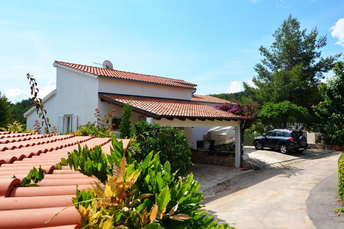 A white building with a red-tiled roof, a covered carport, and a parked car.