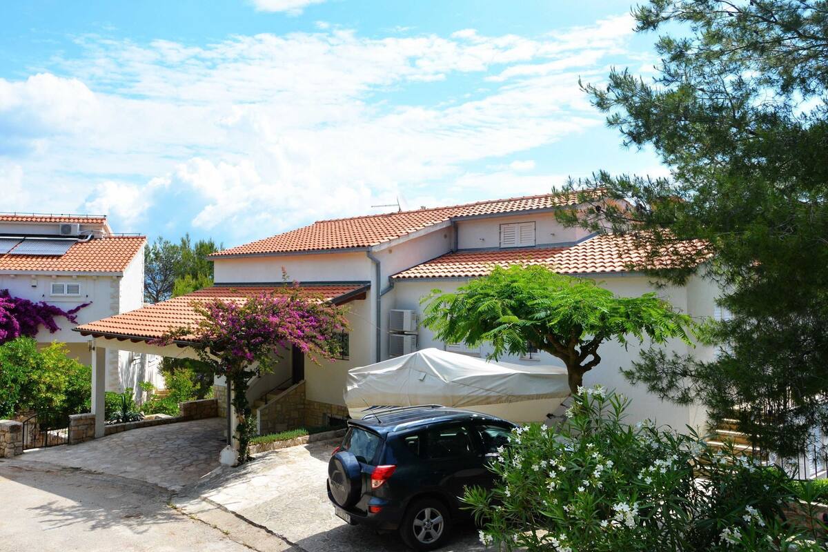 A residential area with houses featuring red-tiled roofs, a parked car, and lush greenery.