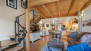 A spacious living area with a wooden staircase, a sofa, a coffee table, and a kitchen in the background. - Pool, Hot Tub, Tennis and Golf, Amazing Views! (Durango)