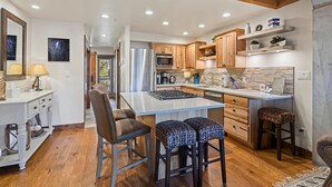 A modern kitchen with wooden cabinets, a large island with stools, and a view of the outdoors. - Pool, Hot Tub, Tennis and Golf, Amazing Views! (Durango)
