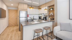 A modern kitchen with wooden cabinets, a built-in refrigerator, a central island with stools, and pendant lighting. - StayShort - Elegant Studio in Rokane G25 Good for 2 (Dubai)