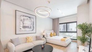 A modern hotel room with a sofa, a bed, a round coffee table, and a large window offering a city view. - StayShort - Elegant Studio in Rokane G25 Good for 2 (Dubai)