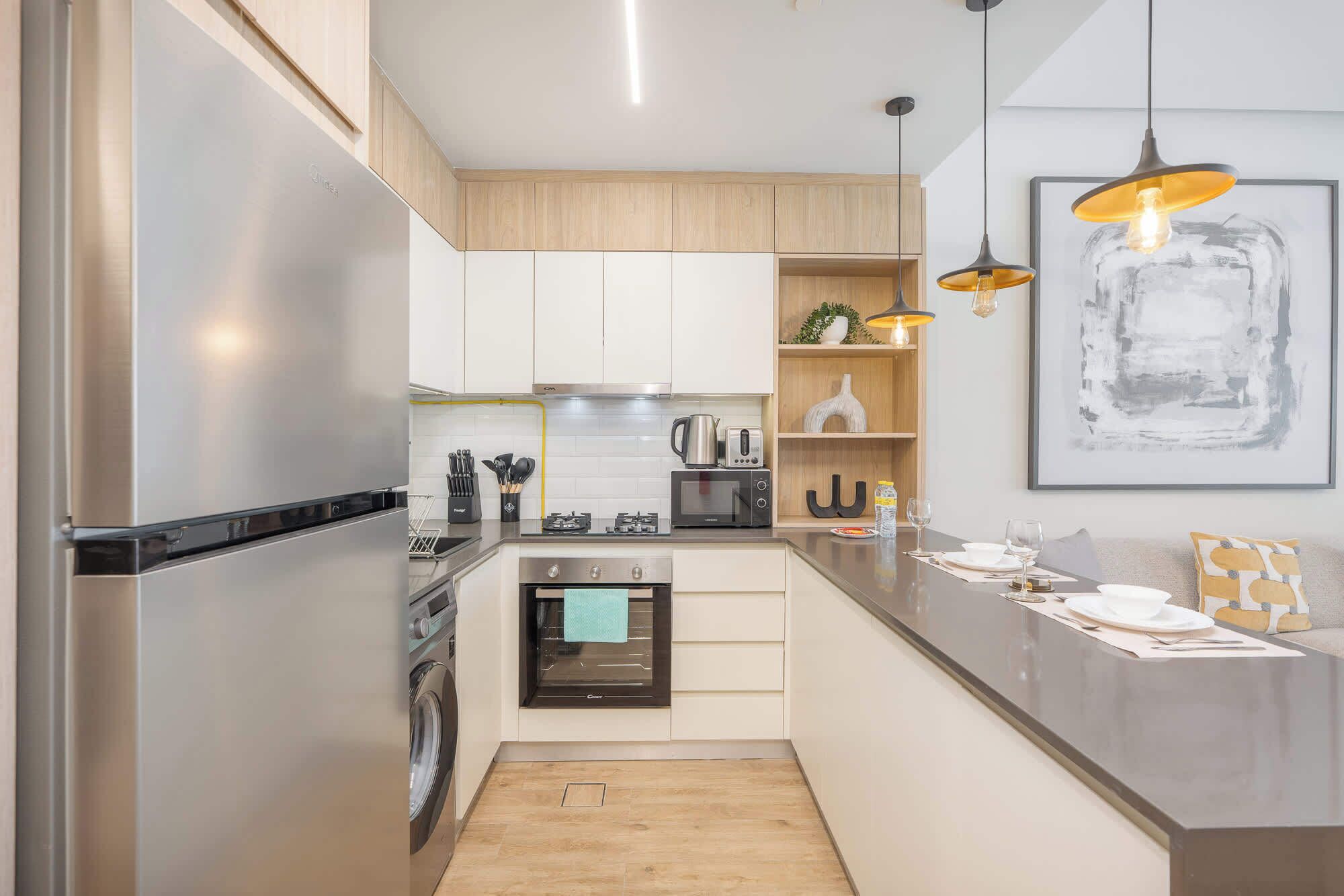 A modern kitchen with stainless steel appliances, wooden cabinets, and pendant lighting.
