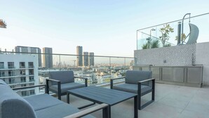 A rooftop terrace with modern furniture, a glass balustrade, and a city view. - StayShort - Elegant Studio in Rokane G25 Good for 2 (Dubai)