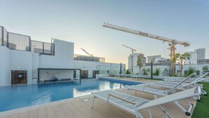 A rooftop pool area with lounge chairs, a clear sky, and construction cranes in the background. - StayShort - Elegant Studio in Rokane G25 Good for 2 (Dubai)