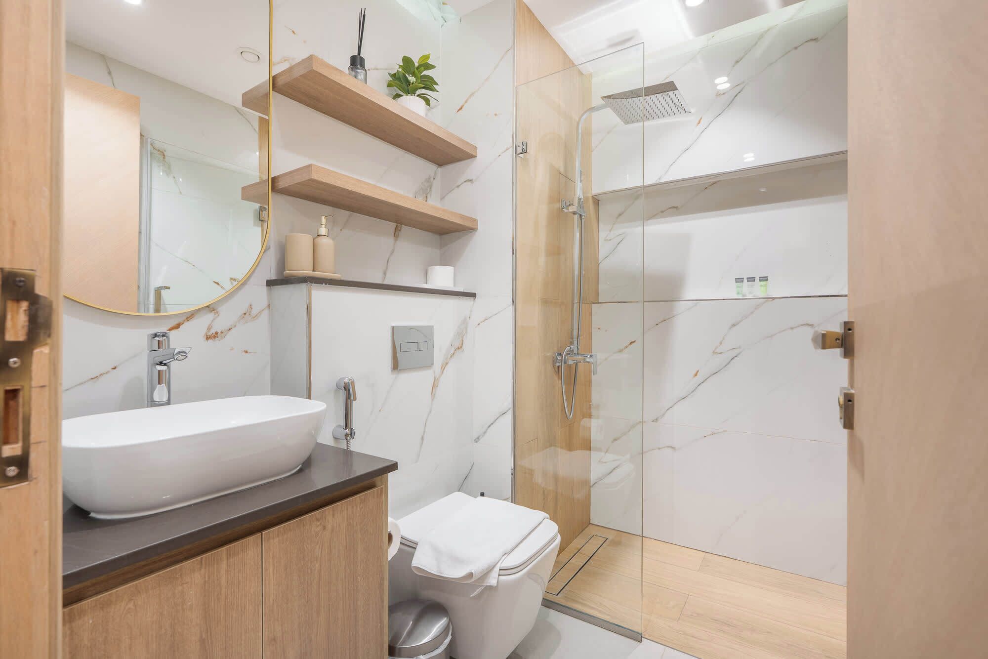 A modern bathroom with a white sink, wooden shelves, a glass shower enclosure, and a marble backsplash.