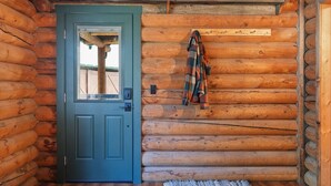 A log cabin interior with a blue door, wooden walls, and a plaid blanket hanging on the wall.